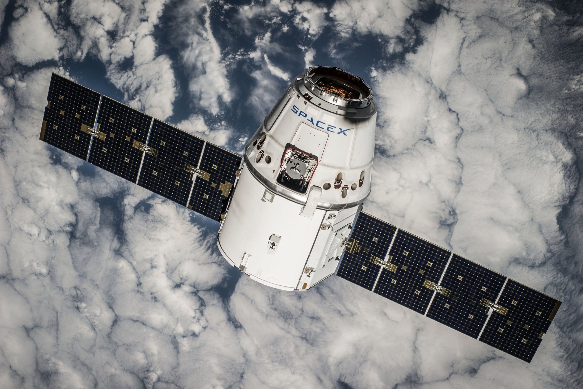 Cargo Dragon spacecraft by SpaceX with extended solar arrays like a satellite, orbiting above cloud-covered Earth — 2K Quad HD PC desktop wallpaper highlighting space technology.