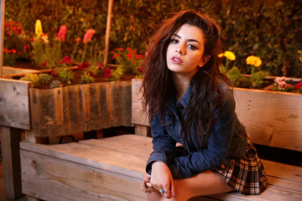 Charlotte Emma Aitchison, also known as Charli XCX, poses outdoors on a wooden bench surrounded by vibrant flowers, featured in an HD music-themed desktop wallpaper.