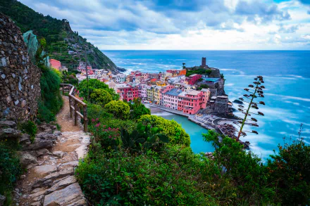 Scenic view of Italy’s Cinque Terre coast in Liguria, featuring colorful seaside buildings, a rocky beach, and a cloudy horizon, captured in HD for a desktop wallpaper.
