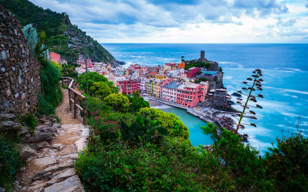 Scenic view of Italy’s Cinque Terre coast in Liguria, featuring colorful seaside buildings, a rocky beach, and a cloudy horizon, captured in HD for a desktop wallpaper.