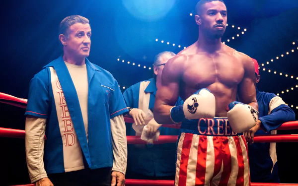 Adonis Creed in striped trunks stands ready in a boxing ring beside Rocky Balboa, corner crew behind him — Creed II 2K Quad HD PC desktop wallpaper