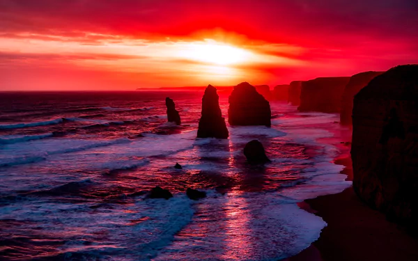 Sunset over the ocean at The Twelve Apostles along the coastline of Victoria, Australia, with vibrant red and orange hues illuminating the sky and water.