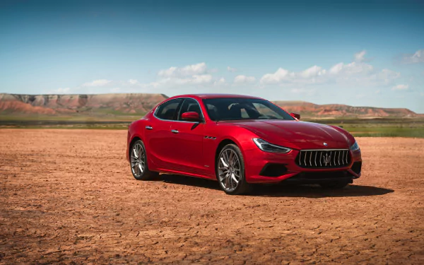 4K Ultra HD PC desktop wallpaper: red Maserati Ghibli grand tourer vehicle parked on cracked desert plain beneath a bright blue sky.