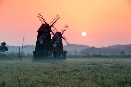 4K Ultra HD wallpaper showing two man-made windmills amid foggy fields at sunrise with a soft pink and orange sky.