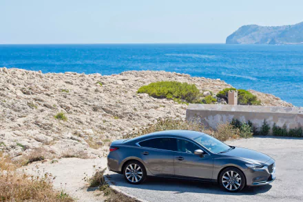 Silver Mazda 6 sedan parked near rocky coastline with ocean and distant cliffs, captured in 4K Ultra HD quality as a PC desktop wallpaper.