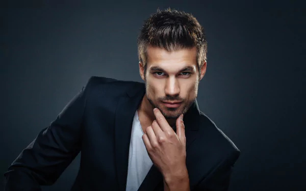 Male model with brown eyes staring at camera, hand on chin, wearing a dark blazer — 5K Ultra HD PC desktop wallpaper/background.