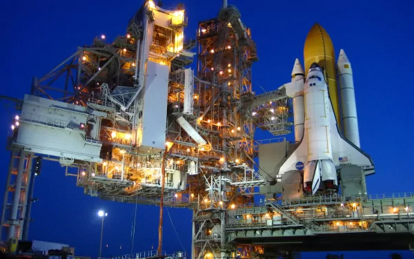 A stunning HD desktop wallpaper of the Space Shuttle Atlantis, illuminated at night and ready for launch, showcasing its detailed structure against a deep blue sky.
