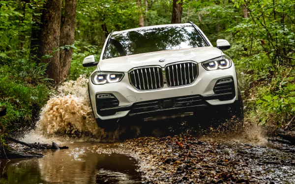 White BMW X5 SUV splashes through a muddy forest trail, captured in a 4K Ultra HD desktop wallpaper showcasing its rugged off-road capability.