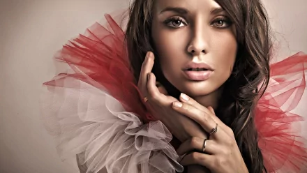 A striking HD desktop wallpaper featuring a pretty woman with captivating eyes, adorned in a ruffled red and white outfit, elegantly posing with her hands by her face.