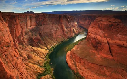 A stunning HD wallpaper of the Grand Canyon, showcasing majestic red rock formations and the winding river below, surrounded by a vibrant sky. A true celebration of nature's beauty.