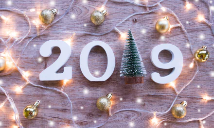 A 4K Ultra HD New Year 2019 desktop wallpaper featuring white numbers, a small Christmas tree, golden baubles, and festive string lights on a wooden background.