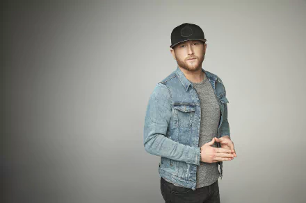A stylish HD desktop wallpaper featuring country music artist Cole Swindell, captured in a modern look with a denim jacket and a cap against a minimalistic background.