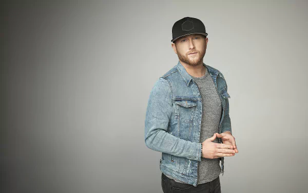 A stylish HD desktop wallpaper featuring country music artist Cole Swindell, captured in a modern look with a denim jacket and a cap against a minimalistic background.