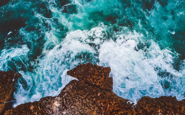 Aerial view of turquoise ocean waves crashing against rugged rocks, captured in stunning 4K Ultra HD nature and water desktop wallpaper.