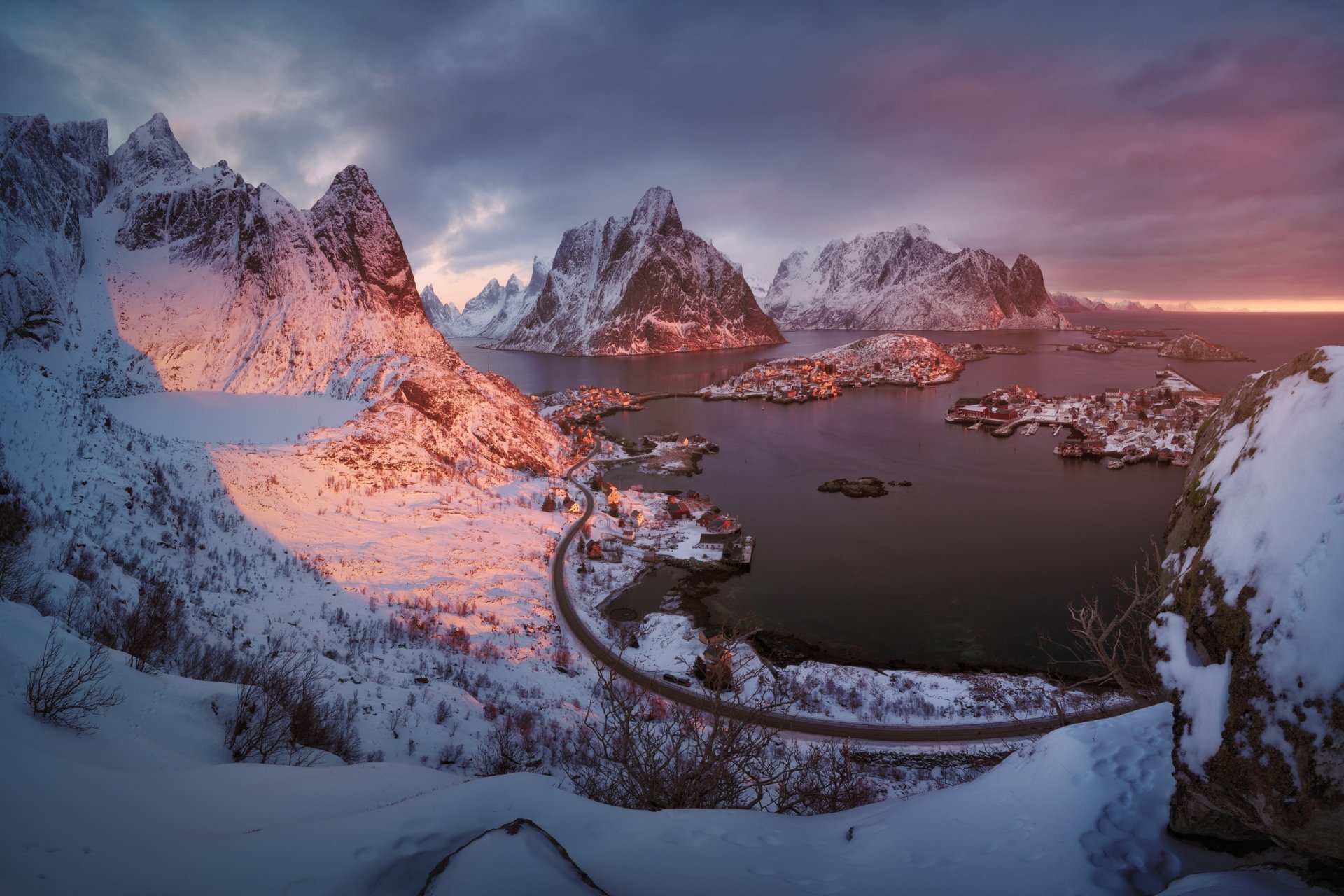 Photography of snow-covered Lofoten mountains and fjord at sunrise, a winding bridge and coastal village — HD PC desktop wallpaper and background.