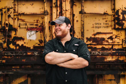 HD desktop wallpaper background featuring a smiling man in a cap posing before a rustic metal backdrop.