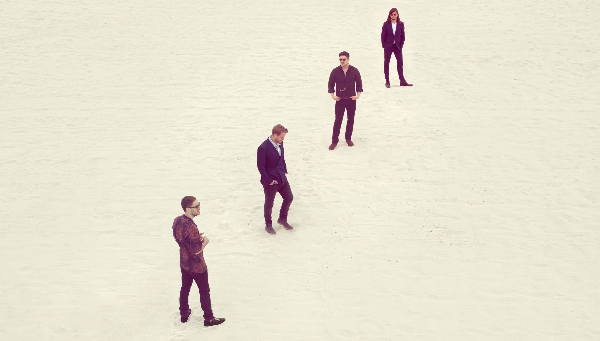 A high-definition desktop wallpaper featuring Mumford & Sons, showcasing the band members standing in a minimalist, open landscape.