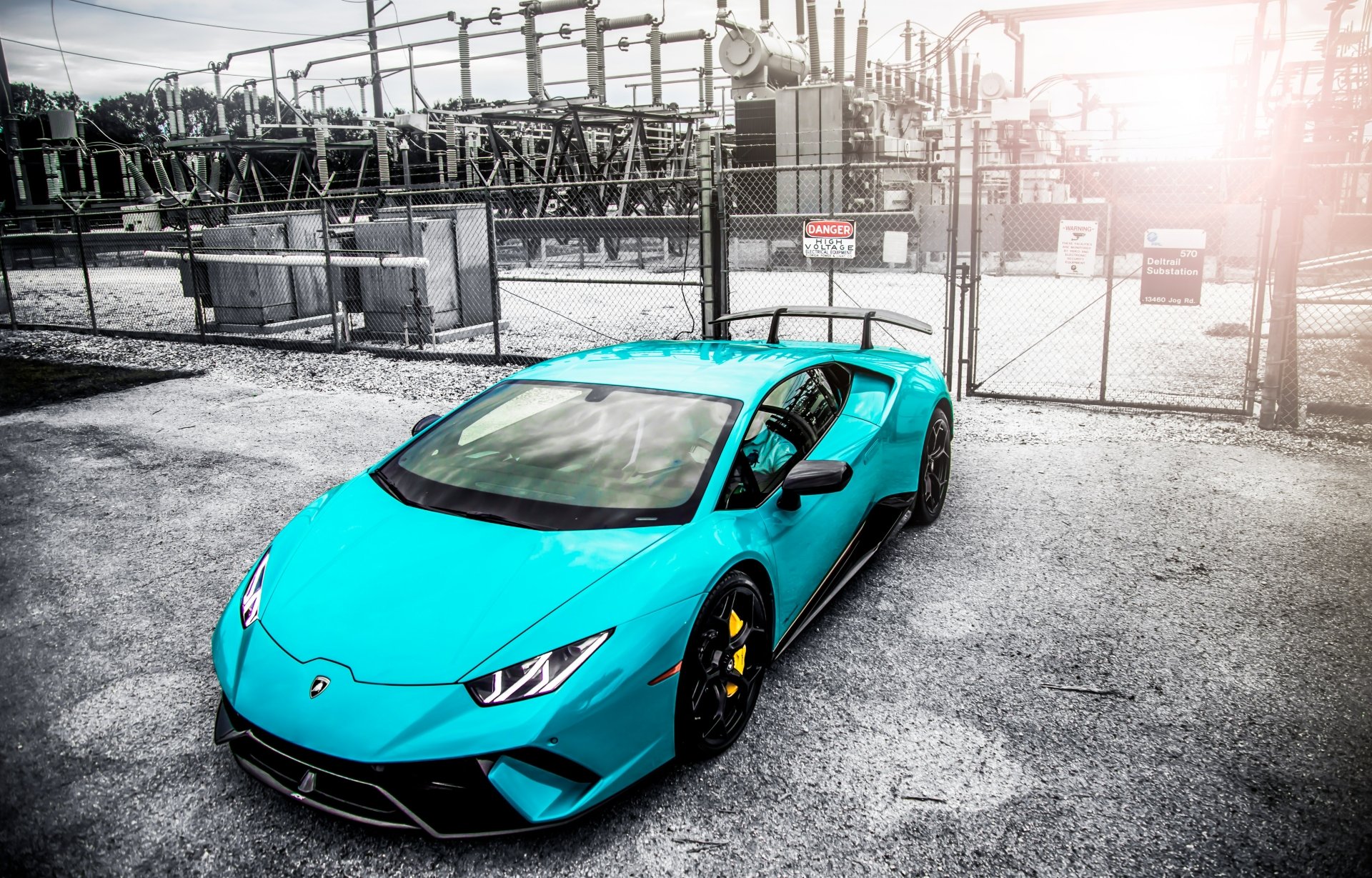 Turquoise Lamborghini Huracan Performante sports vehicle parked in an industrial lot with chain-link fence and sun flare — 5K Ultra HD PC desktop wallpaper and background.