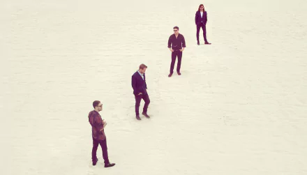 A high-definition desktop wallpaper featuring Mumford & Sons, showcasing the band members standing in a minimalist, open landscape.