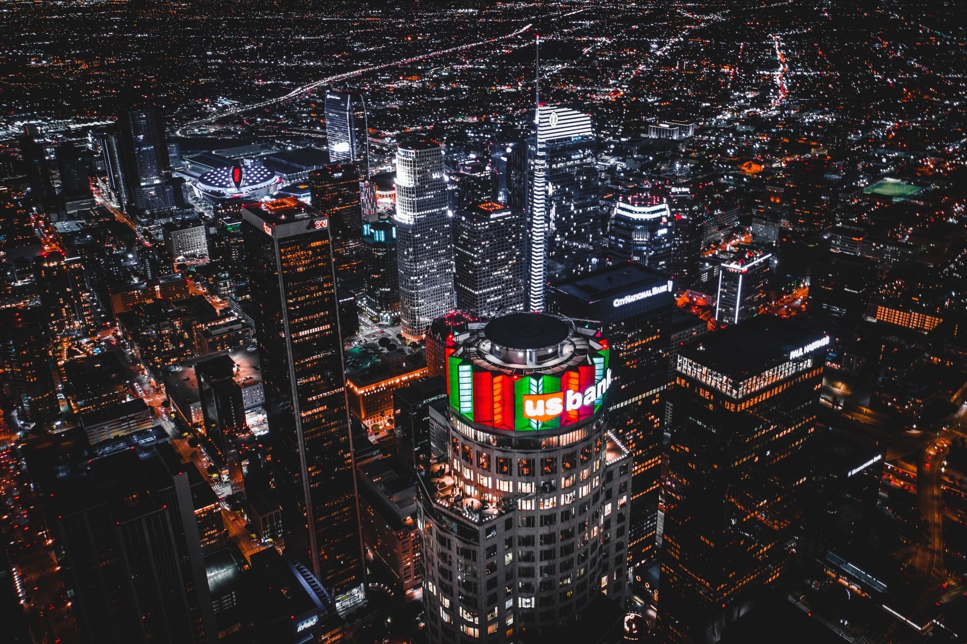 A nighttime aerial view of Los Angeles skyscrapers illuminated with vibrant city lights, showcasing the bustling urban landscape of the USA.