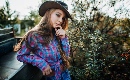 HD desktop wallpaper of a redhead woman model with long hair, blue eyes, wearing a hat and plaid shirt, posing outdoors near greenery.