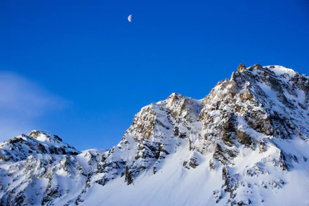 Snow-covered mountain peaks beneath a clear blue sky with a crescent moon, captured in stunning 4K Ultra HD quality.