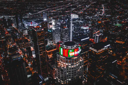 A nighttime aerial view of Los Angeles skyscrapers illuminated with vibrant city lights, showcasing the bustling urban landscape of the USA.