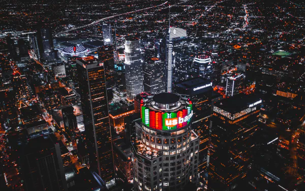A nighttime aerial view of Los Angeles skyscrapers illuminated with vibrant city lights, showcasing the bustling urban landscape of the USA.
