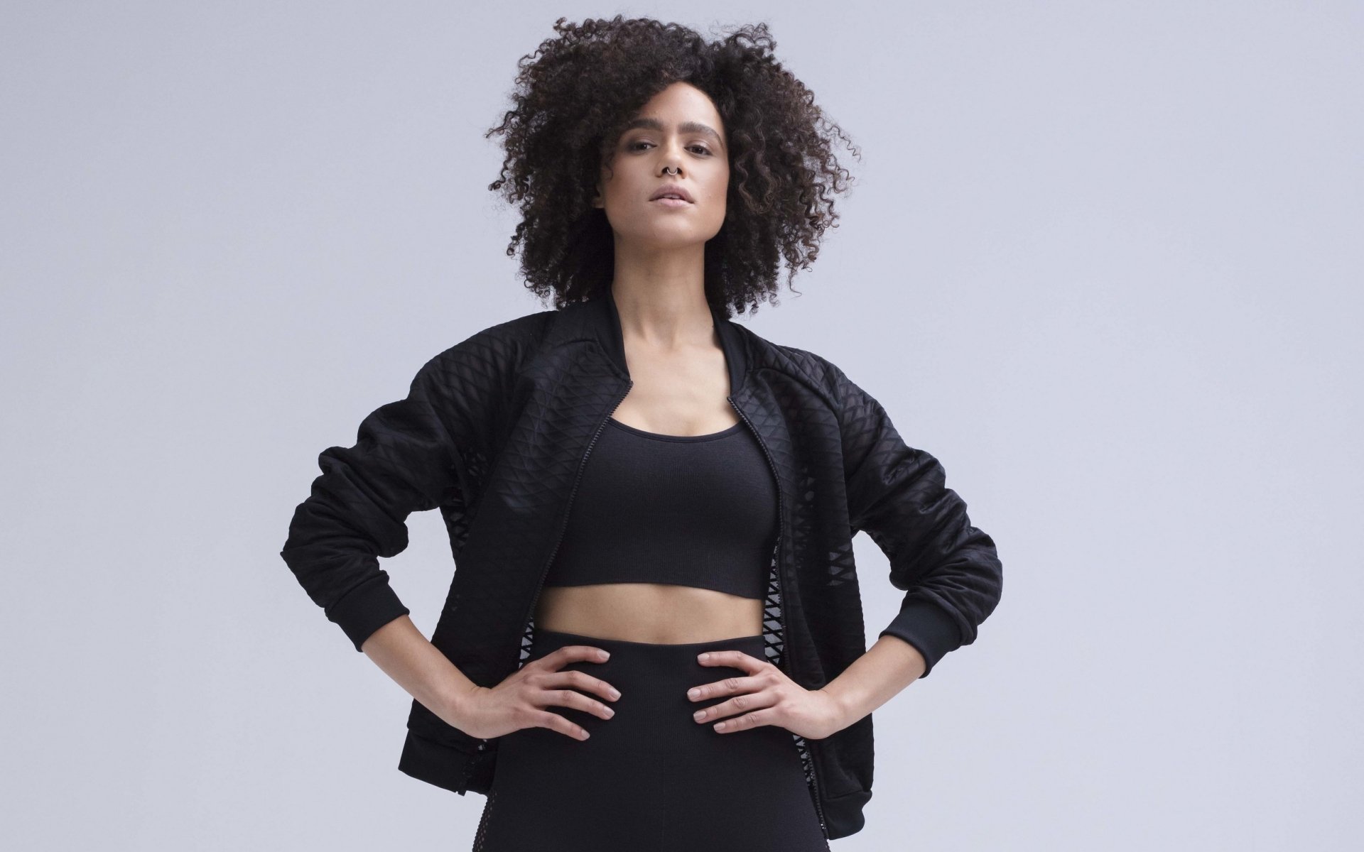2K Quad HD PC desktop wallpaper of a confident English woman with black hair, hands on hips in a black sports bra and jacket against a neutral studio background.