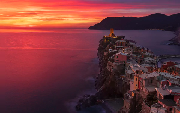 Sunset over Vernazza village in Cinque Terre, with the vibrant horizon casting warm hues over the coastal cliffs and man-made buildings, captured in HD.