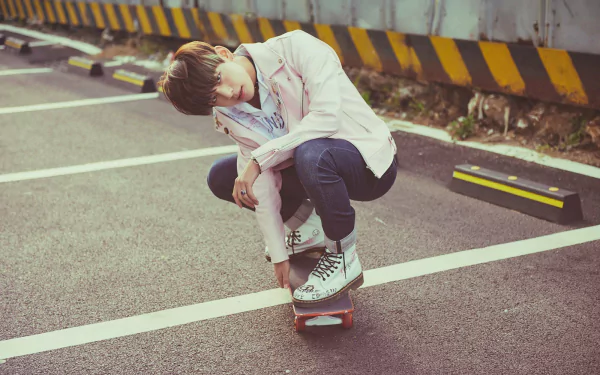 HD desktop wallpaper featuring a member of the K-pop group BTS in casual attire skateboarding in a parking lot with yellow-black striped barriers.
