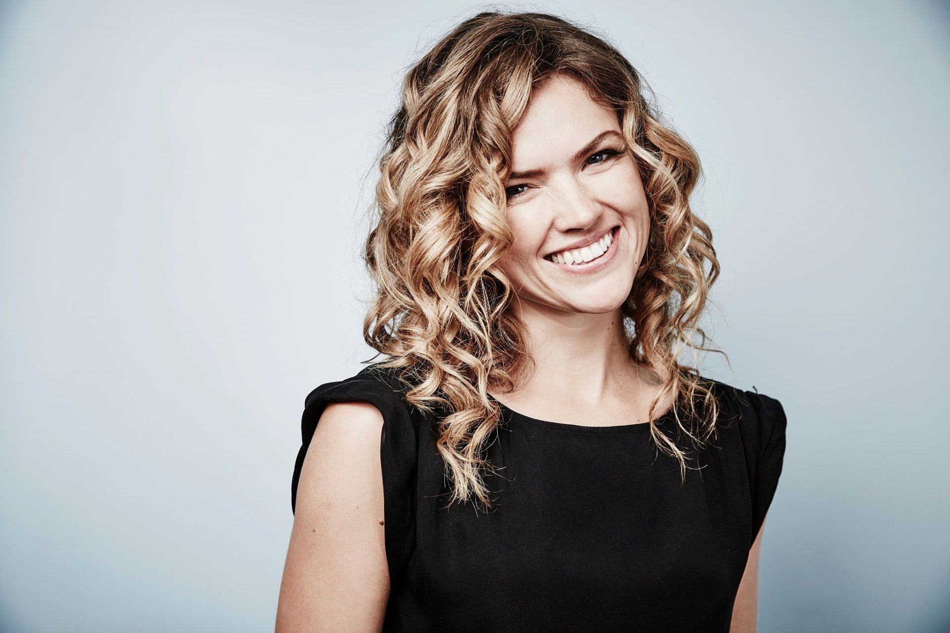 Smiling blonde British woman with curly hair in a black dress, HD PC desktop wallpaper.