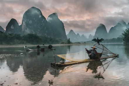 A stunning 4K Ultra HD photograph capturing fishermen with cormorants on calm waters, set against dramatic karst mountains and a moody sky.