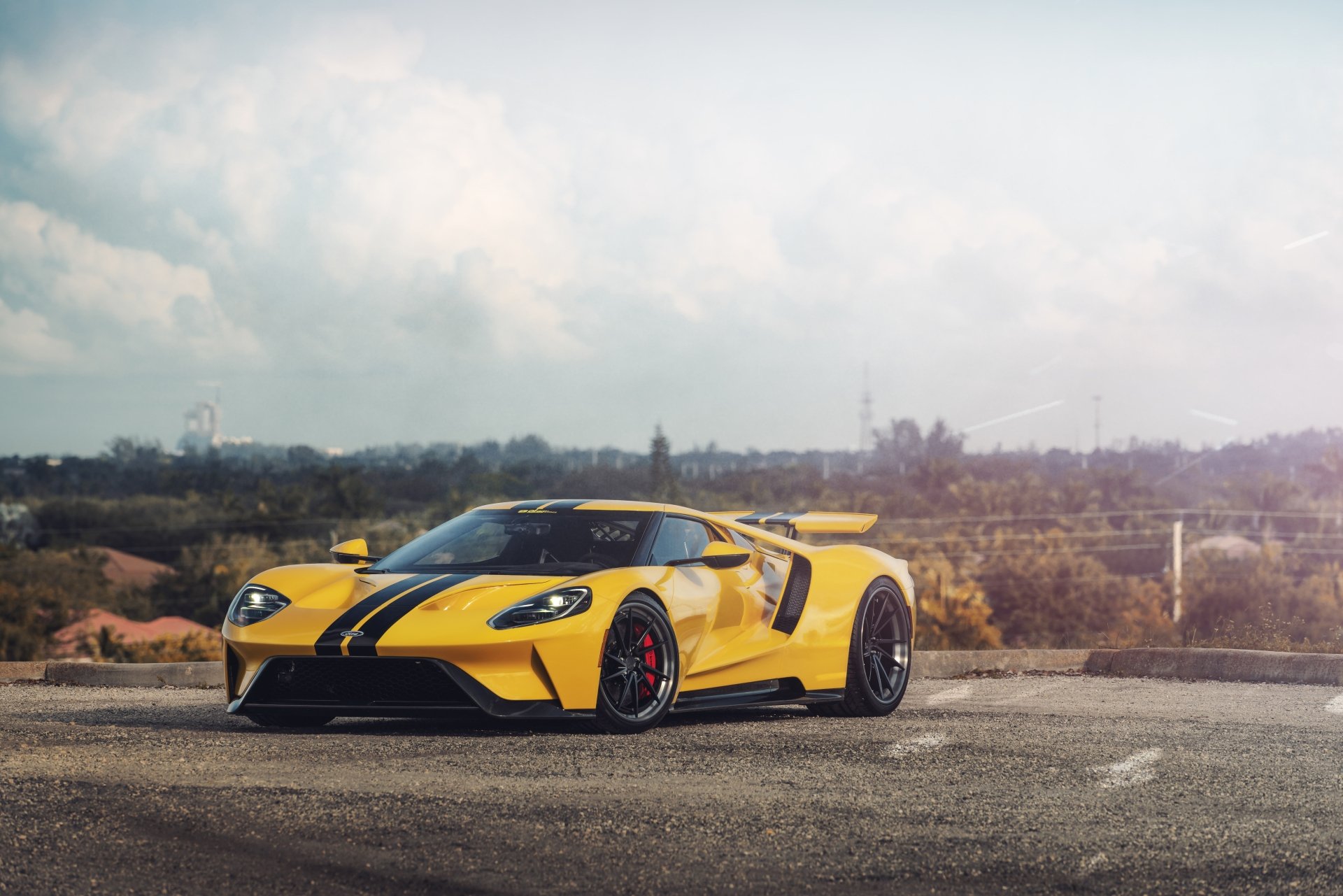Yellow Ford GT supercar with black stripe and red calipers on a scenic overlook — 8K Ultra HD PC desktop wallpaper of a Ford vehicle.