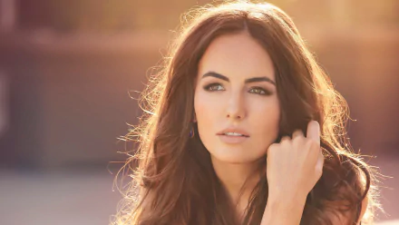 Close-up portrait of a long-haired brunette woman in warm golden light, hand near her face and a serene gaze — 2K Quad HD PC desktop wallpaper.