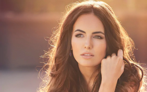 Close-up portrait of a long-haired brunette woman in warm golden light, hand near her face and a serene gaze — 2K Quad HD PC desktop wallpaper.