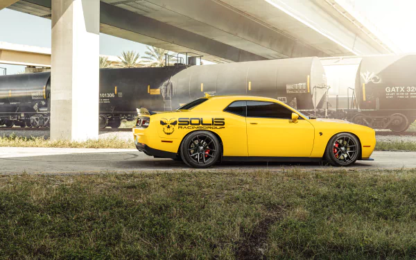 Yellow Dodge Challenger vehicle parked by freight train under an overpass, sunlit industrial backdrop — 8K Ultra HD PC desktop wallpaper and background