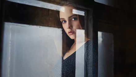 HD desktop wallpaper of a brunette woman model with striking blue eyes, gazing thoughtfully through a window with reflections adding depth to the composition.