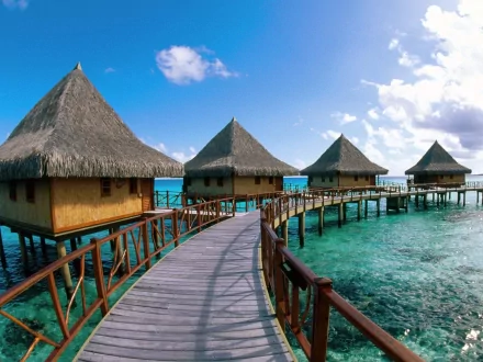 Overwater huts with thatched roofs connected by wooden walkways in the South Pacific, captured in vibrant HD photography for a holiday-themed desktop wallpaper.