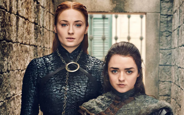 HD desktop wallpaper featuring Sophie Turner as Sansa Stark and Maisie Williams as Arya Stark from the TV show Game of Thrones in a stone-walled setting.