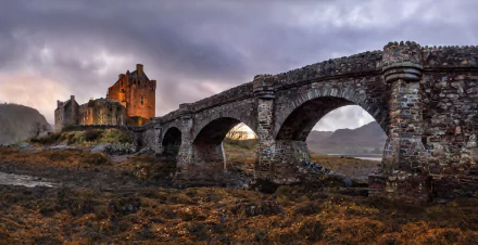 Eilean Donan Castle in Scotland stands beside a stone bridge under a moody sky, captured in a striking HD desktop wallpaper and background scene.