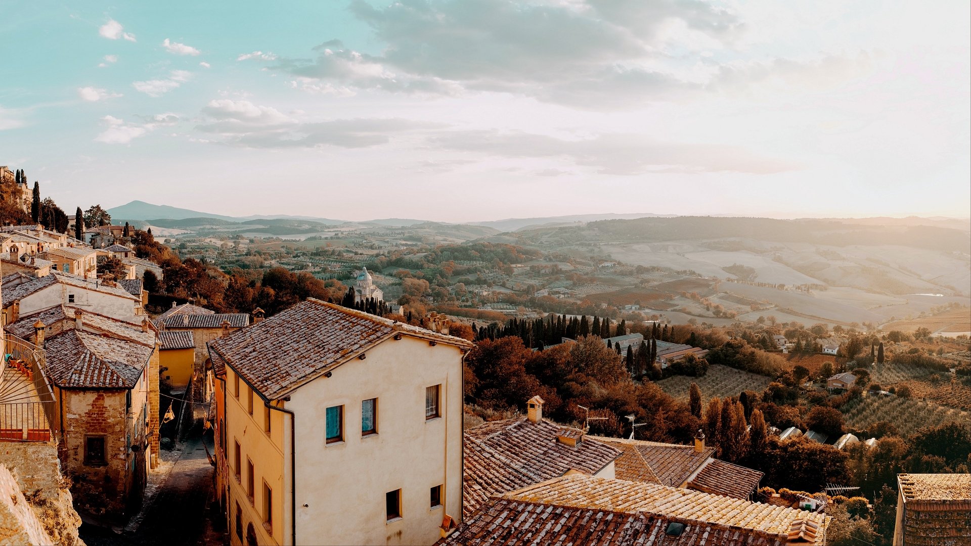 A picturesque man-made village in Italy with rustic rooftops overlooking rolling hills under a bright sky, captured in stunning 4K Ultra HD quality.