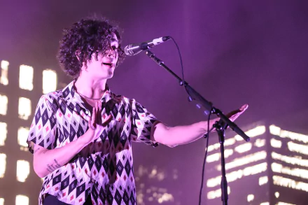HD desktop wallpaper of The 1975 band member performing live with a microphone and colorful stage lights in the background.